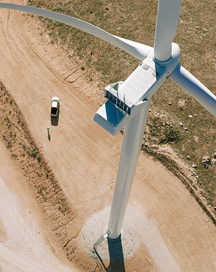 A birds-eye view of the top of a wind turbine with a person walking down a dirt path.