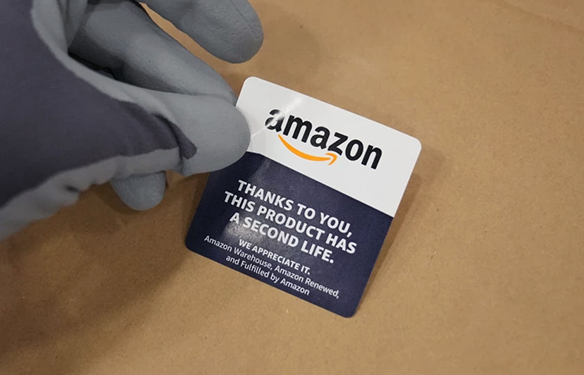 A gloved hand holds a sticker with the Amazon logo over a box. 